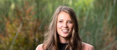 Woman, Annica Schoo, in field, smiling, holding plant, environmental investigator.