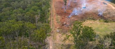 Aerial drone view: Deforestation, half bushland, half cleared land, burning piles, bulldozer.