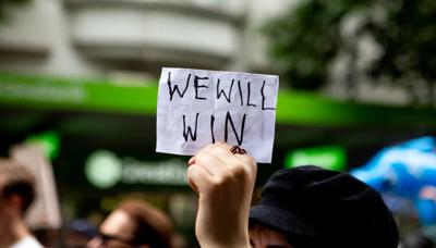 Sign reading "We Will Win" with a hand holding it up.