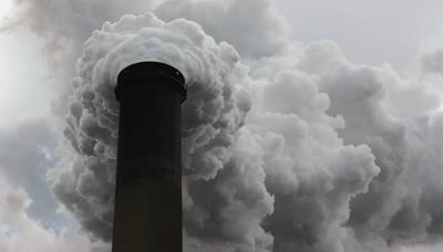 Smoke stack emitting smoke, tall structure against a blue sky.