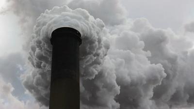 Smoke stack emitting smoke, tall structure against a blue sky.
