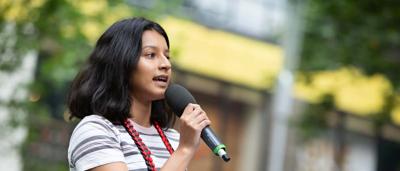 Woman in red coat, holding a camera, standing in a forest, looking at something.