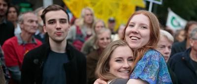 Two people hugging after a rally, one holding a sign.