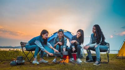 Friends camping, cooking, picnic at sunset. Happy Asian women together.