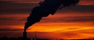 Sunset over polluted cityscape, smog, orange sky, industrial buildings.