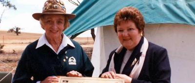 Woman in field, holding shovel, Landcare sign, sunny day.