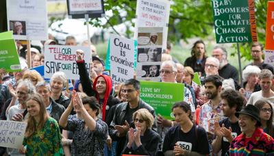 Protest rally banner, crowd, Adani logo, Australian flag, blue sky.