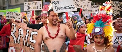 Woman in a red dress, holding a microphone, speaking at a podium. Audience present.