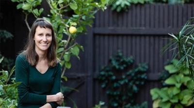 Woman with long hair, smiling, wearing a patterned top, against a blurred background.