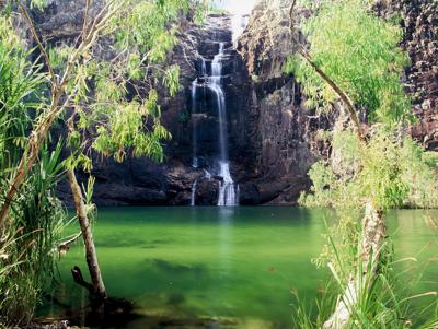 Gunlom Falls waterfall cascading into a creek, lush green surroundings.
