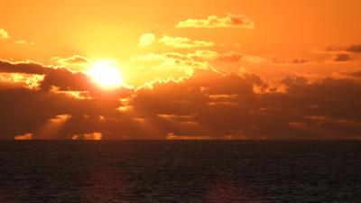 Pacific Ocean sunset over Australia, with sun and clouds.