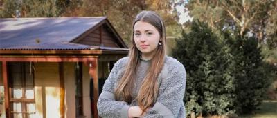 Woman in a forest, holding a seedling, planting it in the ground. Sunlight through trees.