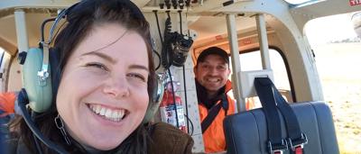 Two people in a helicopter, one piloting, other looking out.