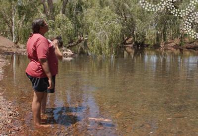 Woman smiling, standing outdoors, trees in background, bright sunlight.