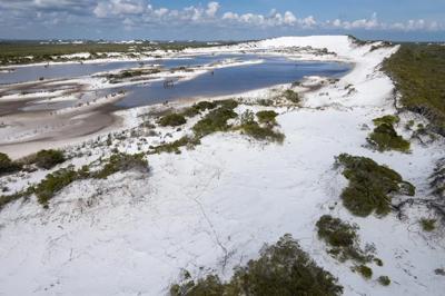 Dune and wetland landscape. Sandy foreground, water, distant hills, blue sky.