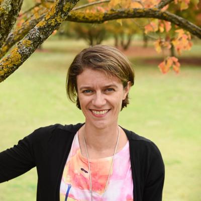 Woman in white coat, holding a clipboard, smiling, in a lab setting.