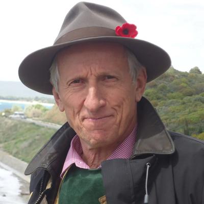 Man in a suit, smiling, outdoors, trees in background, professional headshot.