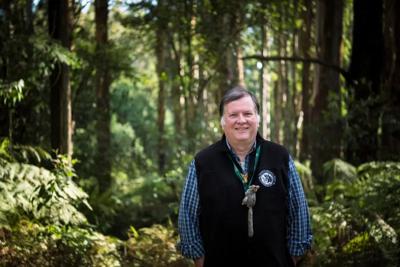 Woman in a field, holding a sign, smiling. Green background, sunny day.