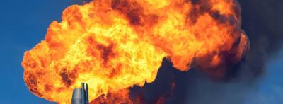 Gas flare at night, orange flames, dark sky, industrial setting.