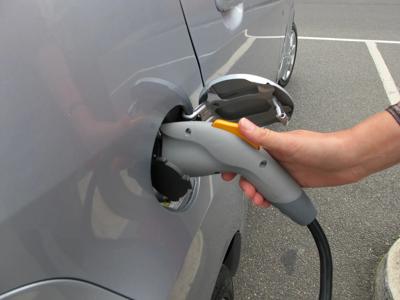 Electric vehicle charging at a station, car plugged in, blue sky.