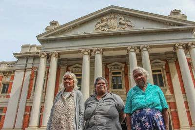 Woman in a white shirt, smiling, holding a microphone, speaking at a podium.