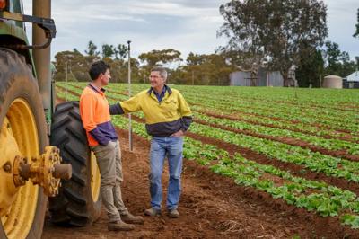 Two men, one with a beard, smiling. Background is a blurred outdoor scene.