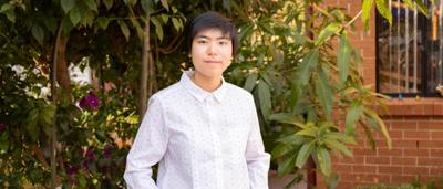Woman smiling, holding a microphone, speaking at a podium with a logo backdrop.