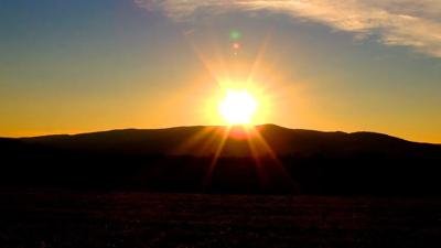 Sunset over ocean, silhouetted trees, orange and purple sky.