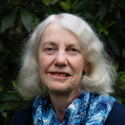 Woman in a white coat, holding a clipboard, smiling, in a lab setting.