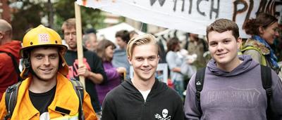 Woman in a white coat, holding a clipboard, looking at a computer screen.