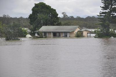 Flooded Taree, NSW. Houses submerged, water covering streets, overcast sky.