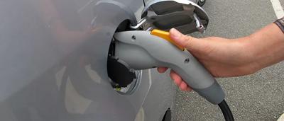 Electric vehicle charging at a station, car plugged in, blue sky.