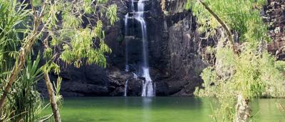 Waterfall cascading down rock face into a pool, lush green vegetation surrounds.