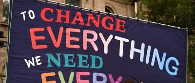 A group of diverse people, some holding signs, gathered outdoors.
