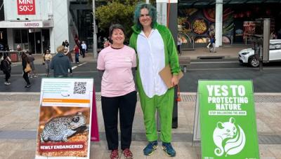 Woman in white shirt, holding a phone, smiling. Background is a blurred office setting.