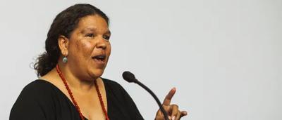 Woman smiling, holding microphone, ICAN logo, background blurred.